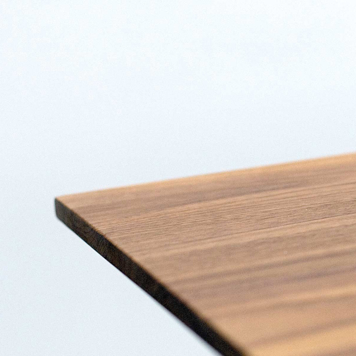 Close-up of a Hussl Solid T Round table corner against a light blue background, showcasing the smooth finish and visible grain patterns of its solid wood tabletop.