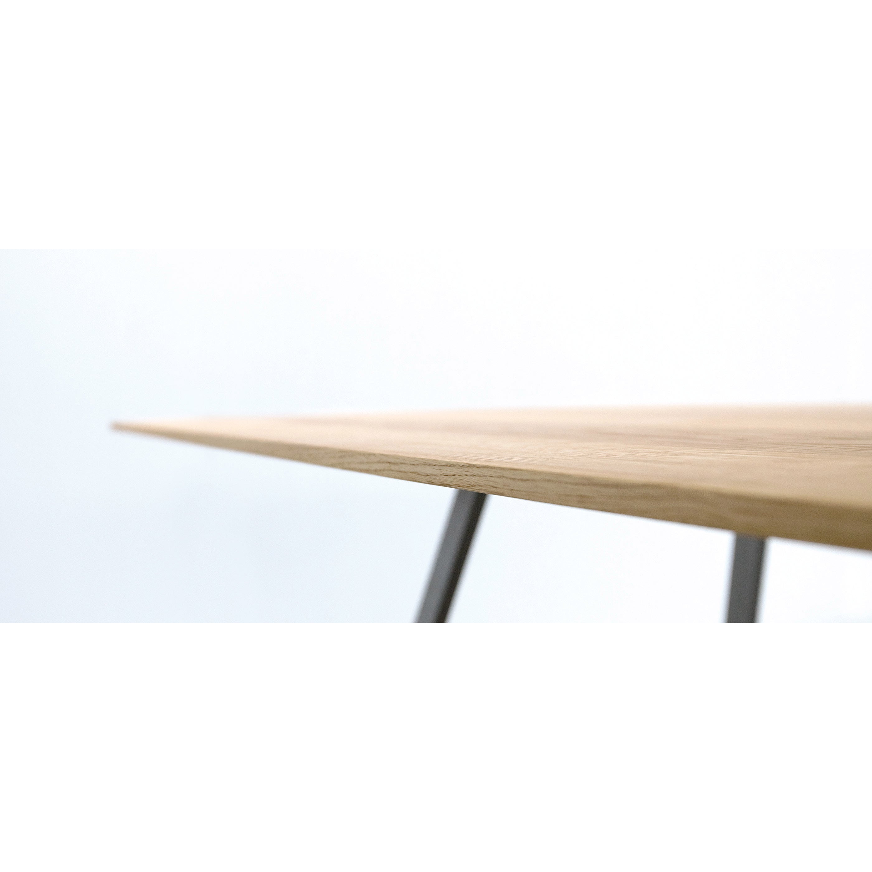 Close-up of the Solid T Rectangular table by Hussl, featuring a sleek floating tabletop with a light wooden surface and slim metal legs, set against a plain white background.
