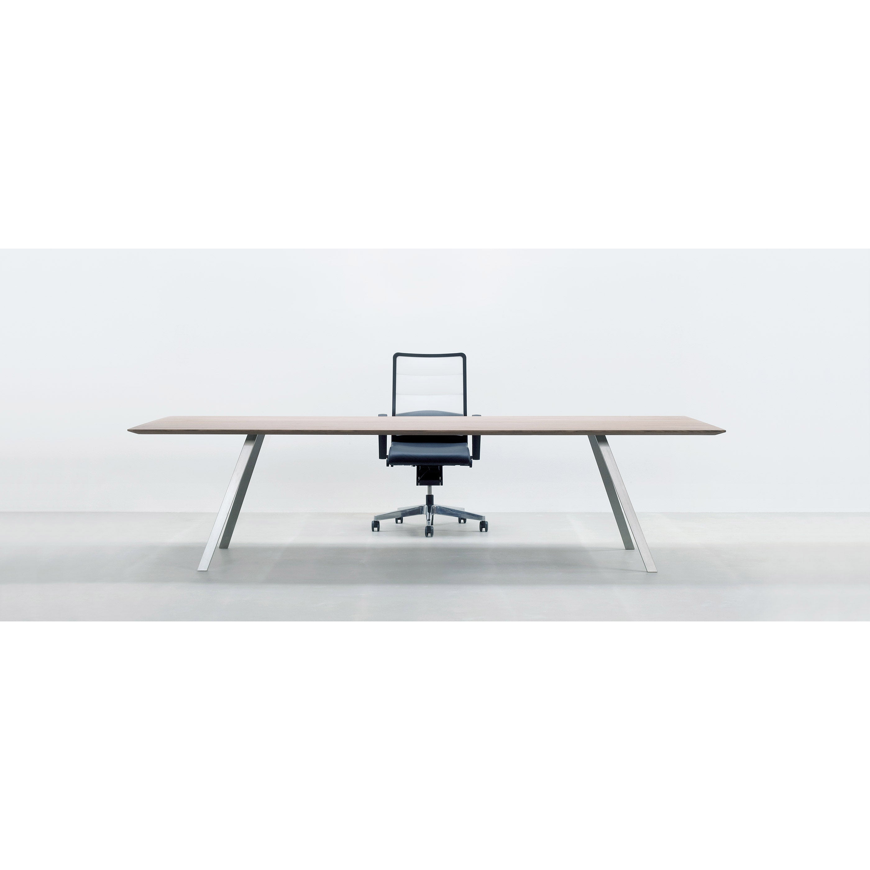 The scene showcases Hussls Solid T Rectangular table, featuring a solid wood tabletop with angled white legs. A black office chair with a mesh backrest stands behind it, all set against a pristine white background.