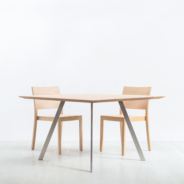 The Solid T Rectangular by Hussl offers a minimalist dining setup with its solid wood tabletop and triangular base design, paired with two matching wooden chairs against a white background for a clean, modern look.