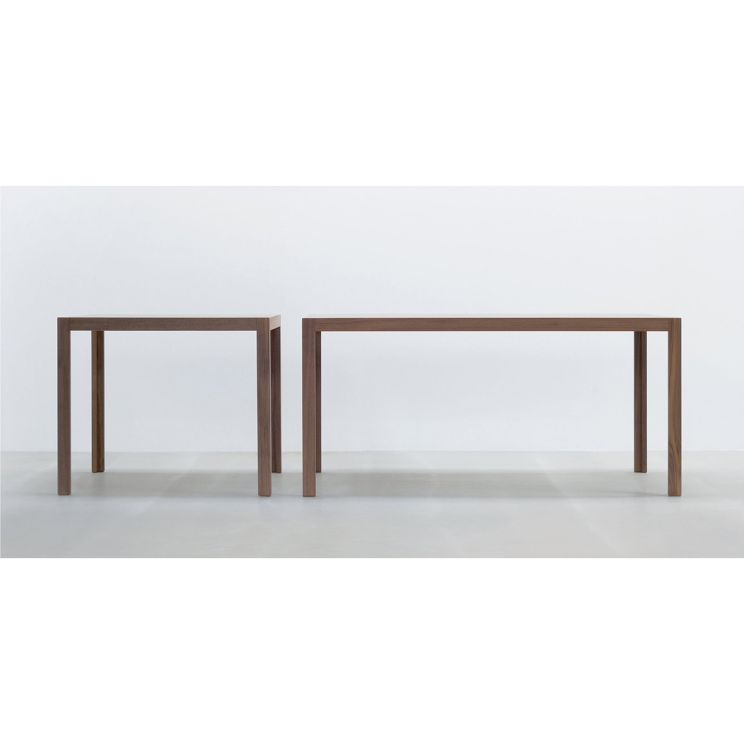 Two TC10 wooden tables by Hussl, featuring minimalist and straight-line designs, stand at different heights on a durable light floor against a white wall, offering a modern aesthetic ideal for business spaces.