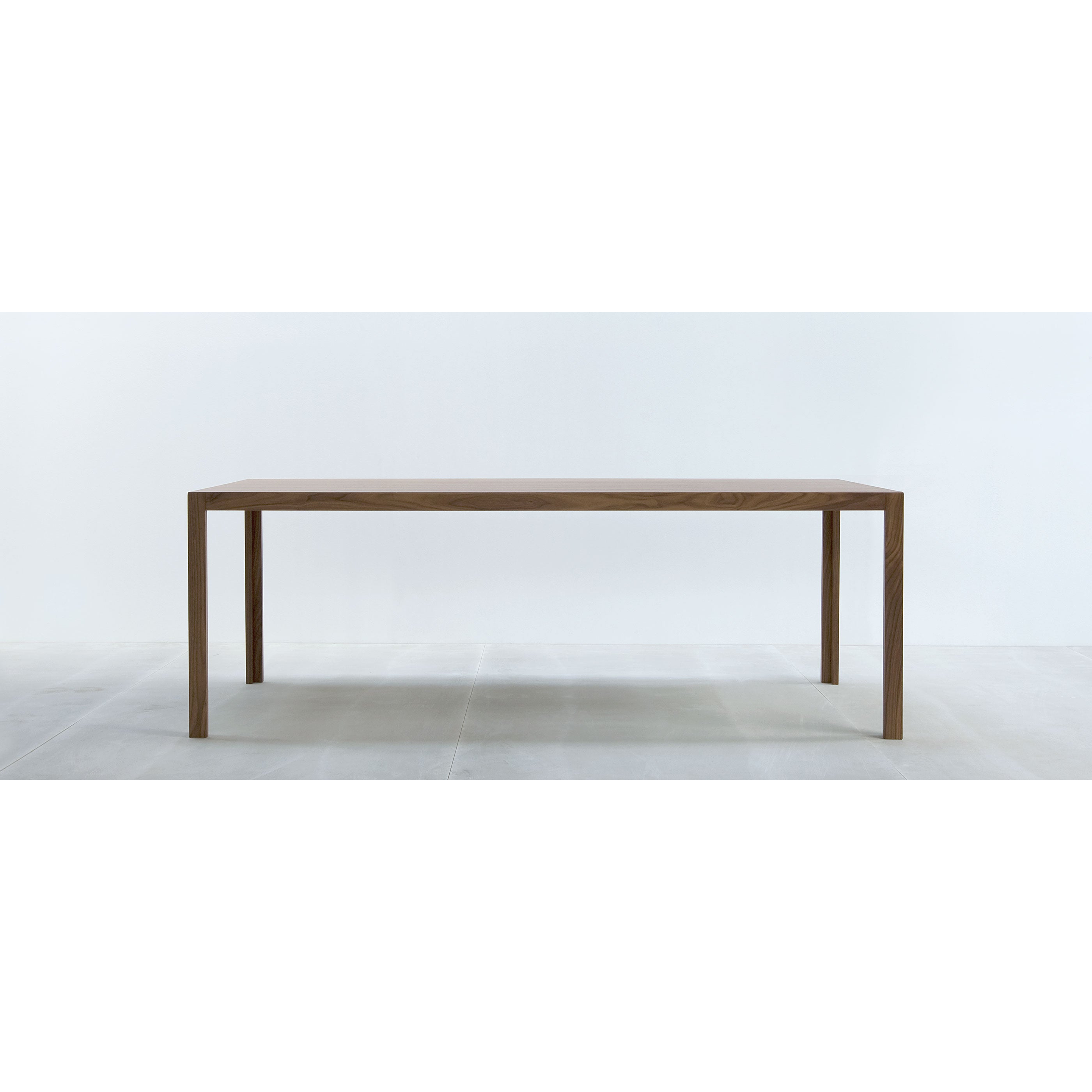 The Hussl TC10 is a minimalist wooden dining table with a rectangular shape and four straight legs. Ideal for business settings, its durable surfaces complement its placement on a light floor against a white wall, offering a contemporary and simple design.