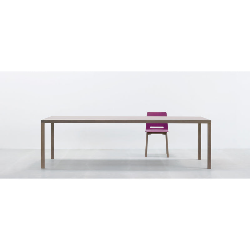 A minimalist room showcases the Hussl TC4, a long, rectangular wooden table paired with a single purple chair, perfect for business settings. The plain white background sharply contrasts with the furnitures durable surfaces.