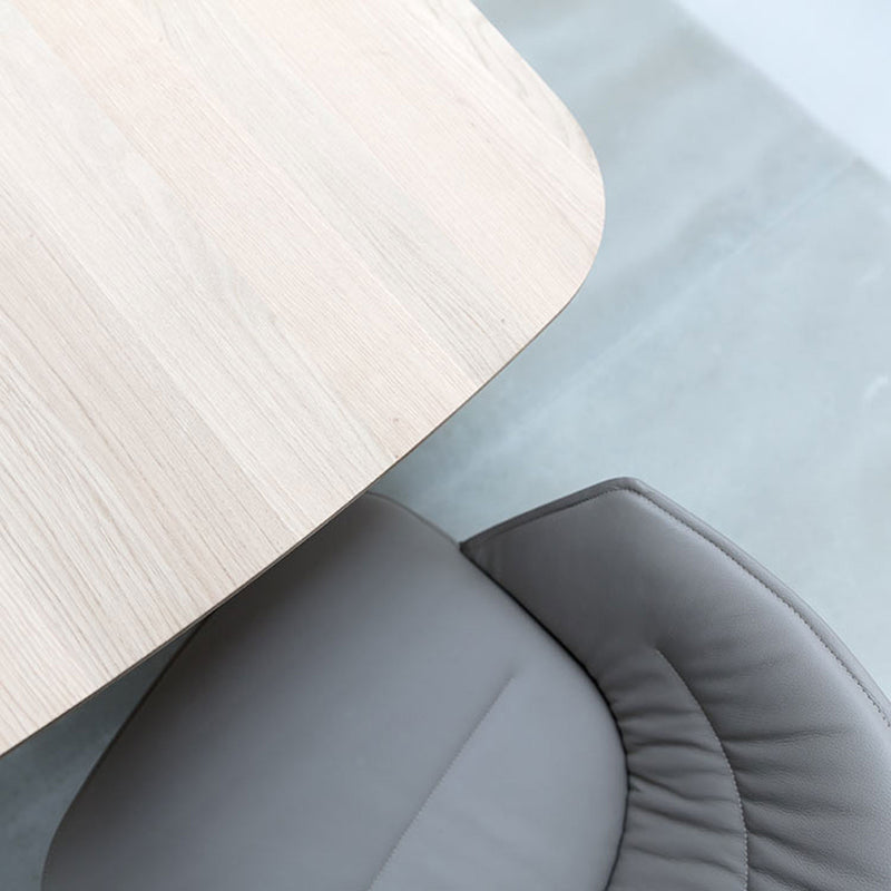 Top view of a light wooden table with rounded edges paired with the Hussl Lino C armchair, featuring an ergonomic design. The chair is partially beneath the table on a light gray floor, enhancing a minimalist and modern aesthetic with natural materials.