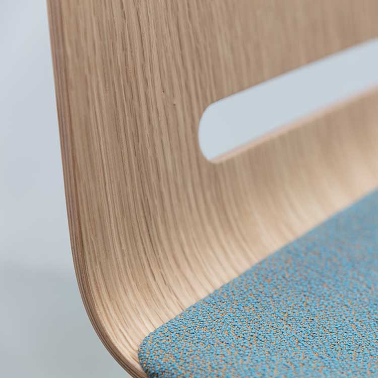 The Forum 2S - Upholstered by Hussl is a modern stackable timber chair with a light wood backrest featuring a horizontal cutout and an upholstered seat in textured blue fabric, enhancing its minimalist design.