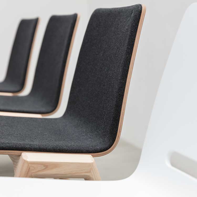 Three Hussl Forum 2S chairs with dark gray upholstery and light wooden frames are arranged in a row. Their minimalist design features clean lines and a smooth finish, standing out stylishly against a light-colored background.