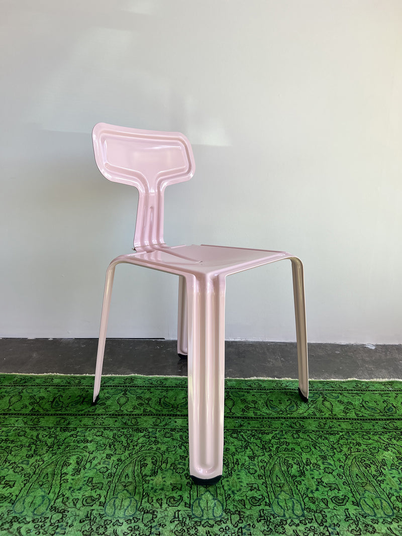 Moormanns Pressed Chair - Sale features a pink metallic finish with angular lines and a unique geometric design, crafted from aluminum. It sits on a green patterned rug against a light gray wall, offering a contemporary look with its shiny surface.