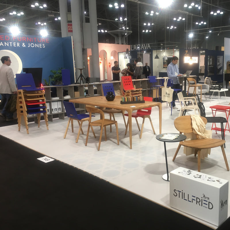 At a modern furniture exhibition booth, Hussls Forum 2S - Ultramarine Sale vibrant chairs are featured alongside wooden tables and decor on carpet. Visitors browse the displays under bright lights in a spacious indoor venue.