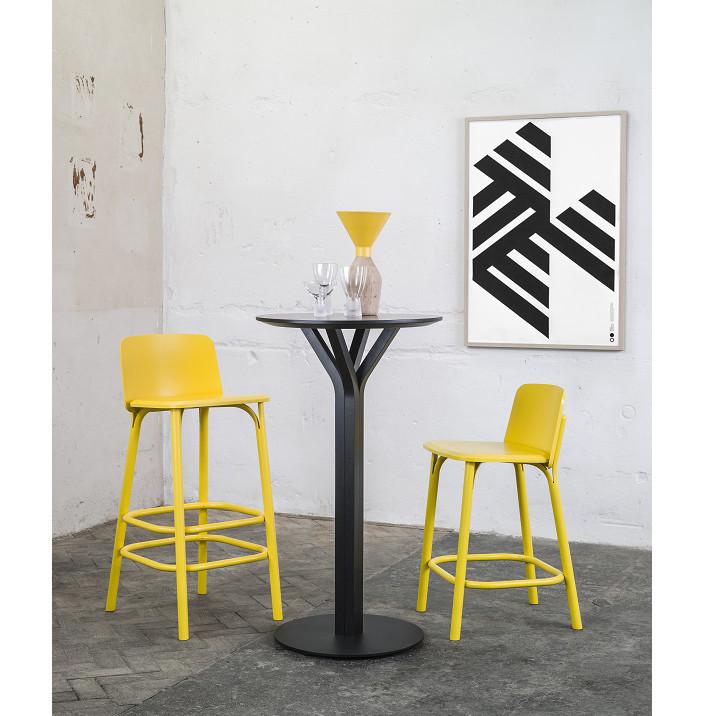 A minimalist room includes the Bloom Bar Table Square by TON, accompanied by two yellow stools. The table features a yellow vase and two glasses that complement the décor. A black and white abstract geometric artwork adorns the white wall, while a simple pattern enhances the gray floor.