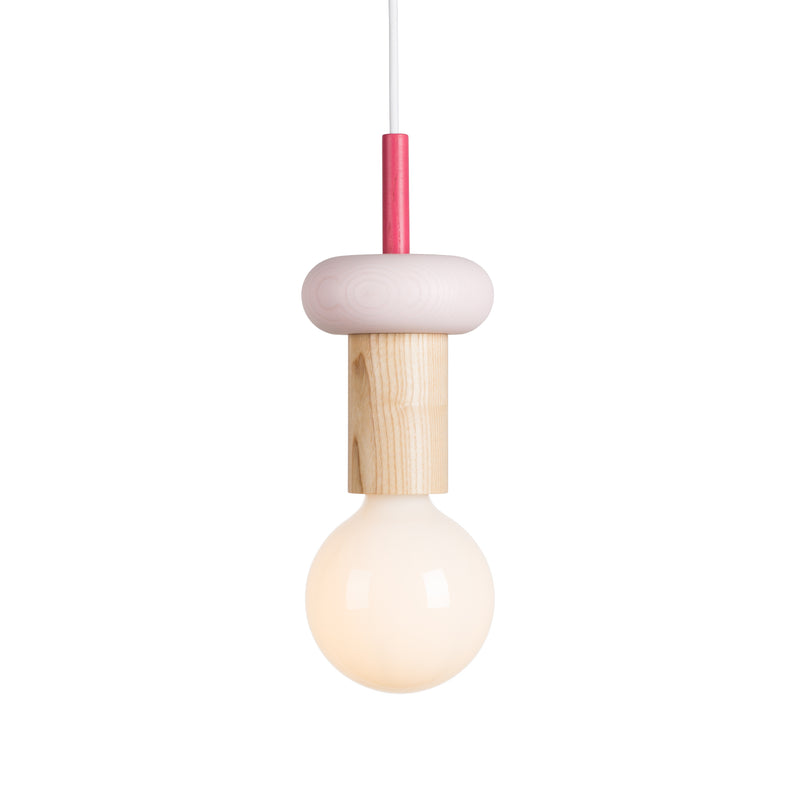 The Junit Drop by Schneid is a modern pendant lamp with a minimalist design. It features a large round bulb, an ash wood cylindrical fixture, and a pink-accented rod. This modular light hangs elegantly from a white cord against a pristine white background.