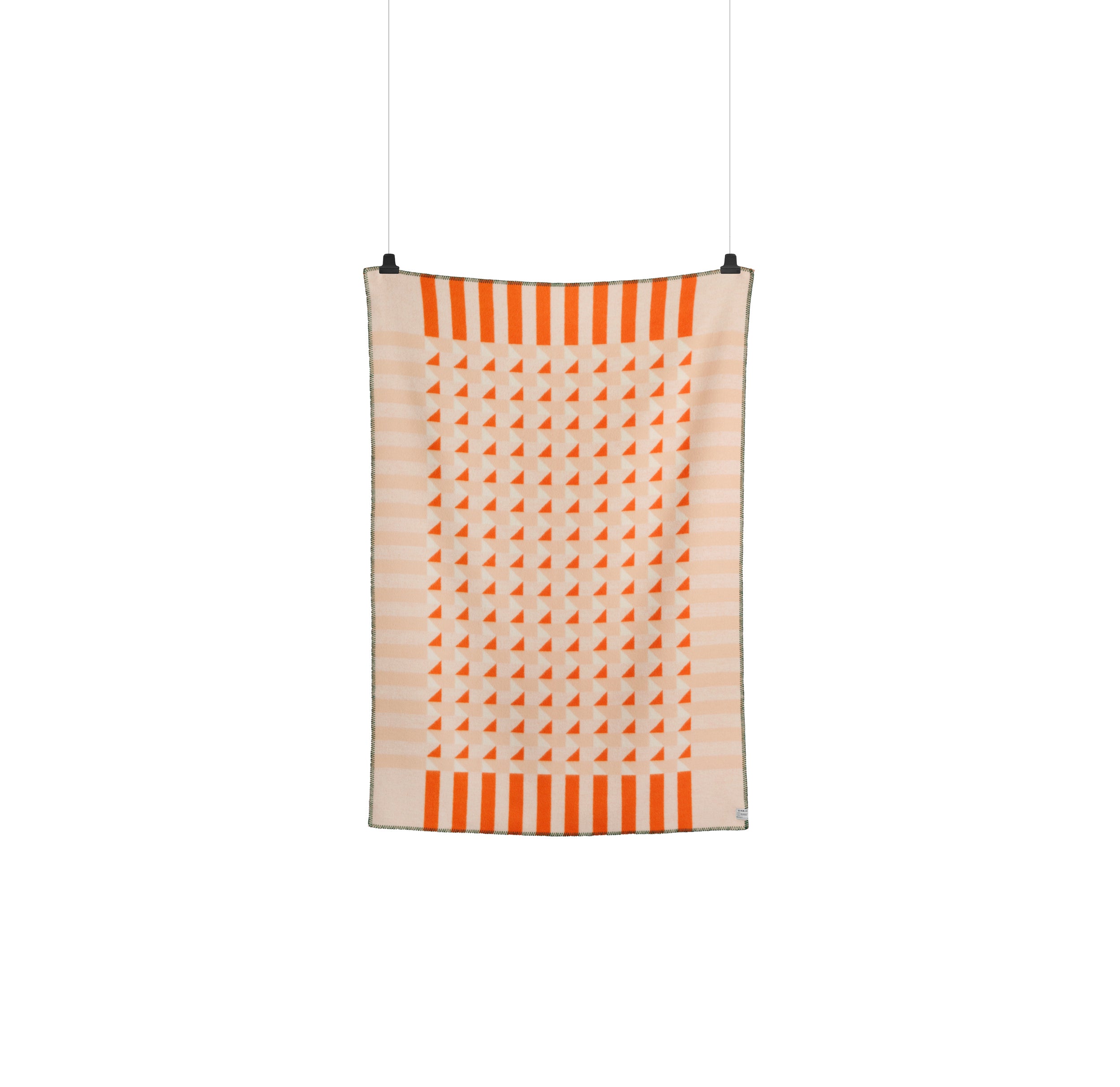 The Kvam Large Throw by Roros is a hanging rectangular blanket made from Norwegian lambswool in a jacquard weave, featuring an orange and white geometric design with central rows of orange triangles and alternating striped edges.