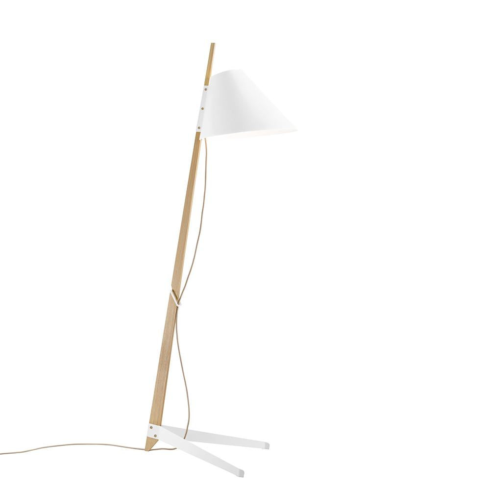 The Billy Floor Lamp by Kalmar features a minimalist design with a wooden stand, lacquered white metal base, and conical lampshade. Its cord runs along the stand, which rests on two angled legs against a plain white background.