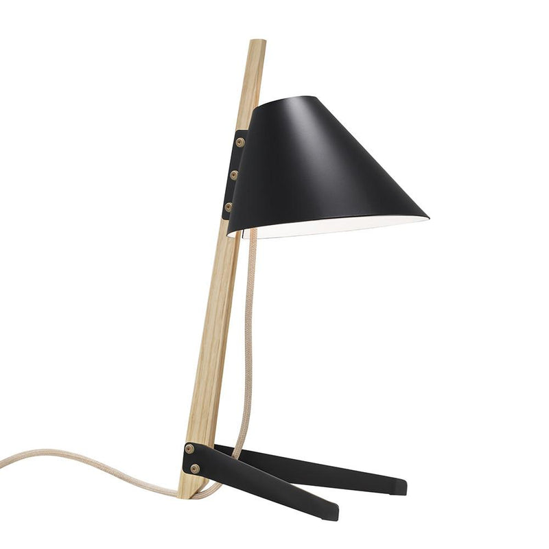 The Billy Table Lamp by Kalmar has a black cone-shaped shade angled downward, featuring a wooden stand and black legs. It comes with a visible beige cord and lacquered metal accents, showcasing a sleek industrial design for a minimalist finish.