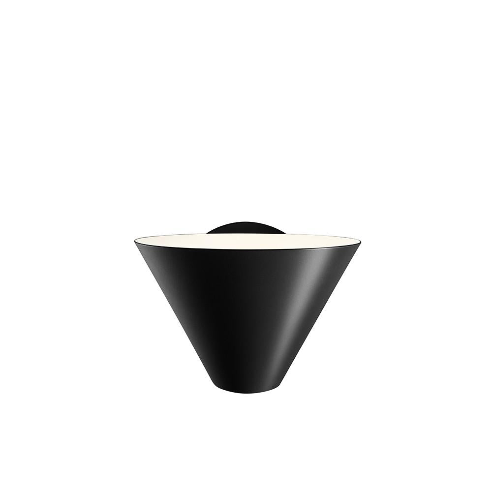 The Billy Wall sconce by Kalmar boasts a minimalist, conical design with a rounded backplate on a white backdrop. It emits light from the wide top of its cone, elegantly contrasting its black exterior and showcasing refined industrial design.