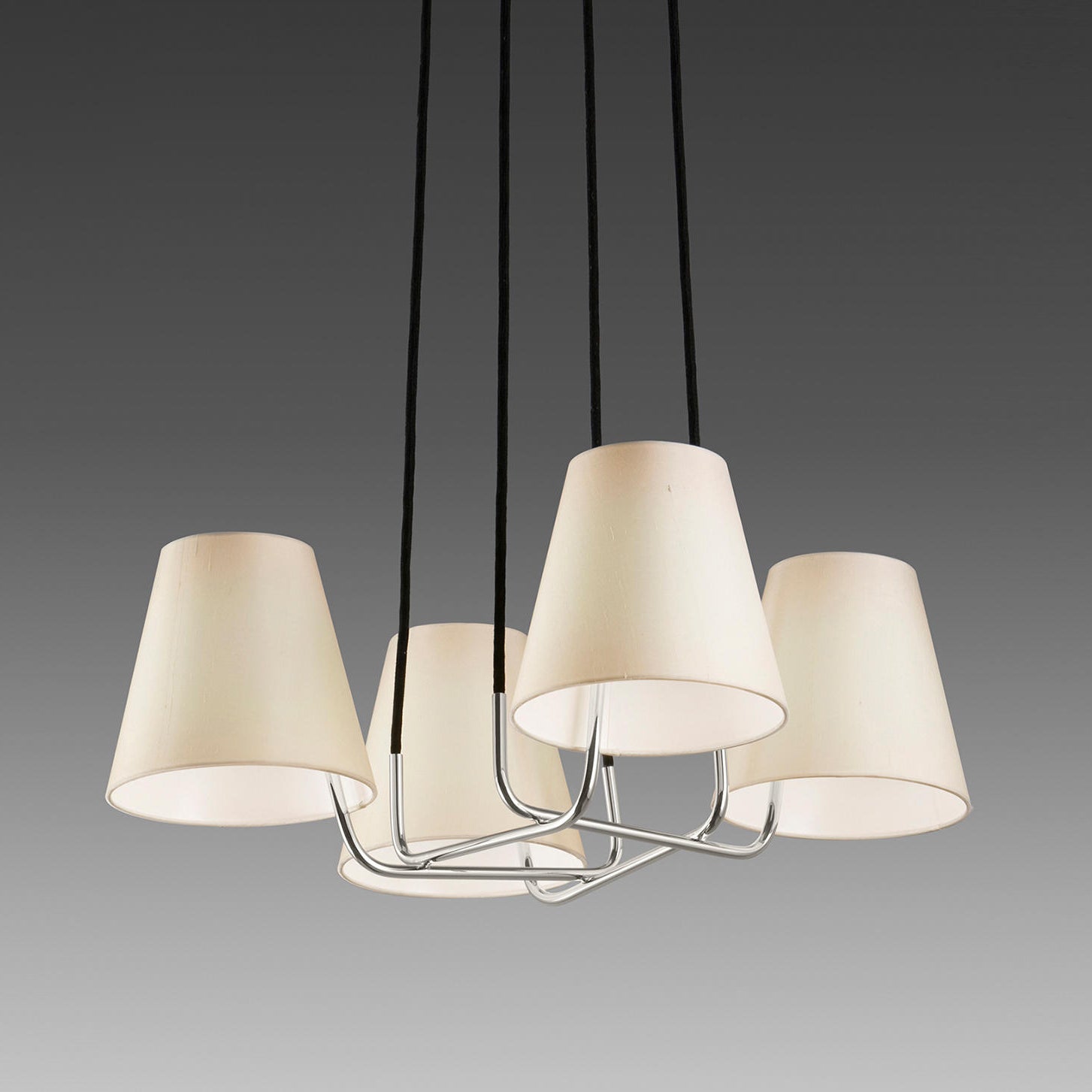 The Kalmar Corona chandelier boasts five cone-shaped, cream silk shades on black cords set against a dark gray background. These elegant lampshades encircle a central chrome fixture, adding an exquisite touch to any room.