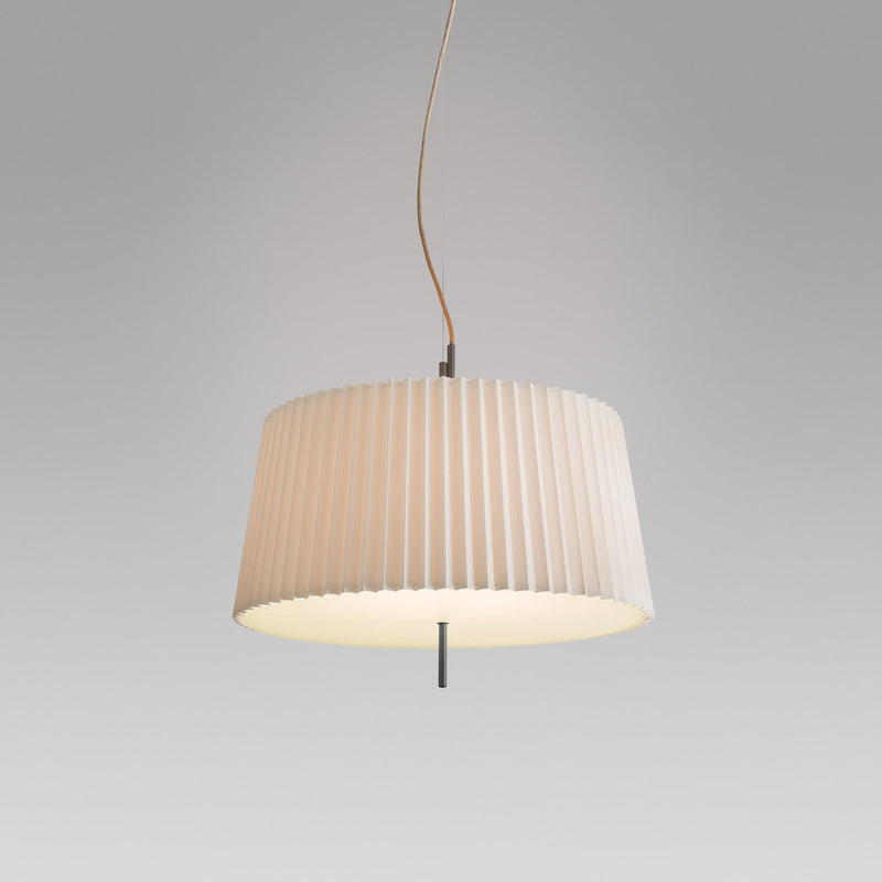 The Fliegenbein HL Pendant by Kalmar boasts a pleated silken shade, blending design elegance with cream-colored charm. It hangs from a slim black rod and brown cord, adding sophistication against a plain gray background.