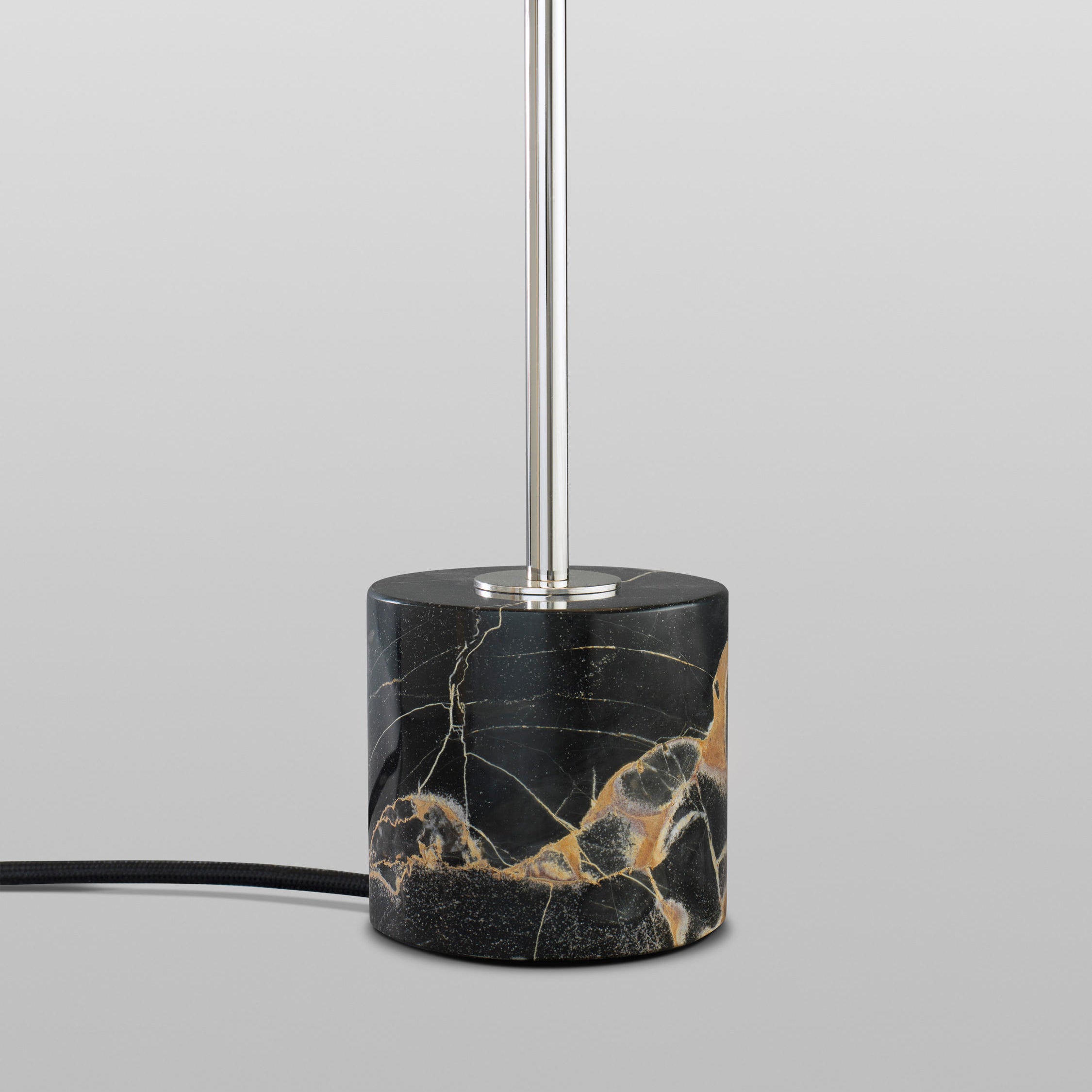 The Kilo Nero Portoro Marble Table Lamp by Kalmar features a base of Nero Portoro marble with gold veining and a sleek vertical metal rod, complemented by a black electrical cord.