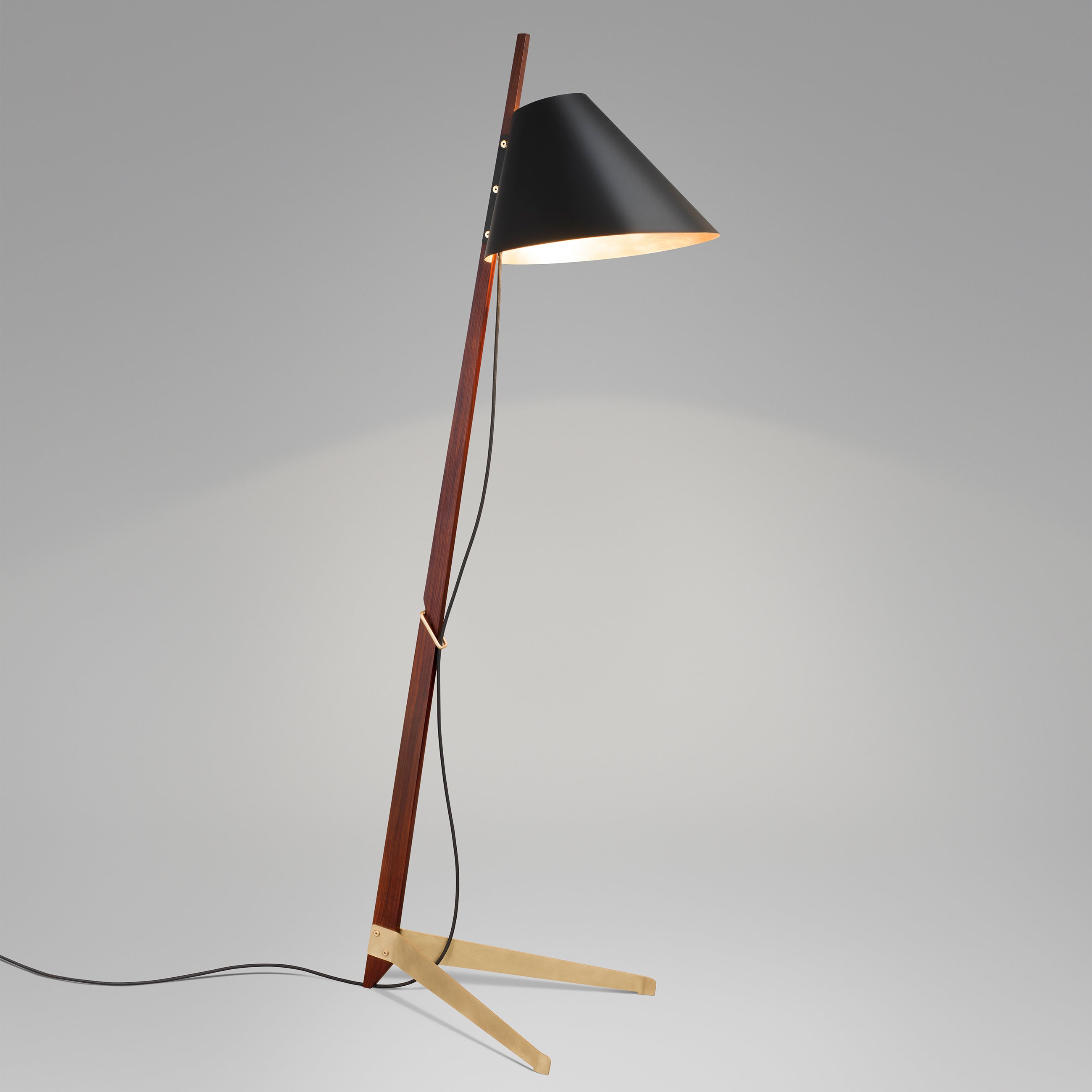 Introducing the Kalmar Billy Floor Ilse Crawford Edition: a modern lamp with a rosewood stem, black conical shade, tilted stand, visible black cord, satin-brass feet, and light wooden base set against a gray background.