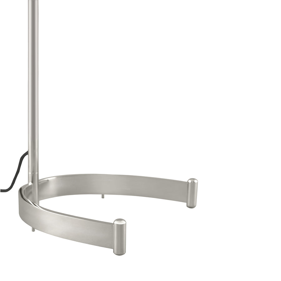 The Egon Floor Lamp by Kalmar features a silver metal base with a modern U-shaped design and three legs. A black power cord is partially visible on the left side, offering directional light for focused illumination against a white floor and background.