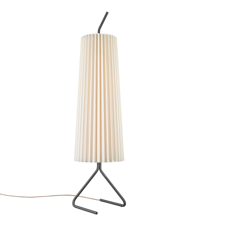 The Fliegenbein SL by Kalmar features a tall, modern design with a pleated silk shade. Its sleek black metal base forms an angular V, and the power cord discreetly emerges from the base, maintaining its minimalist allure.