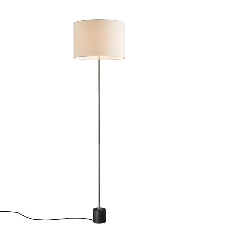 The Kilo Floor Lamp by Kalmar is a modern freestanding luminaire featuring a slender metal pole with a polished nickel finish, a black circular base, and a cream-colored cylindrical lampshade. A black power cord extends from the base, slightly coiled on the floor against a plain white background.