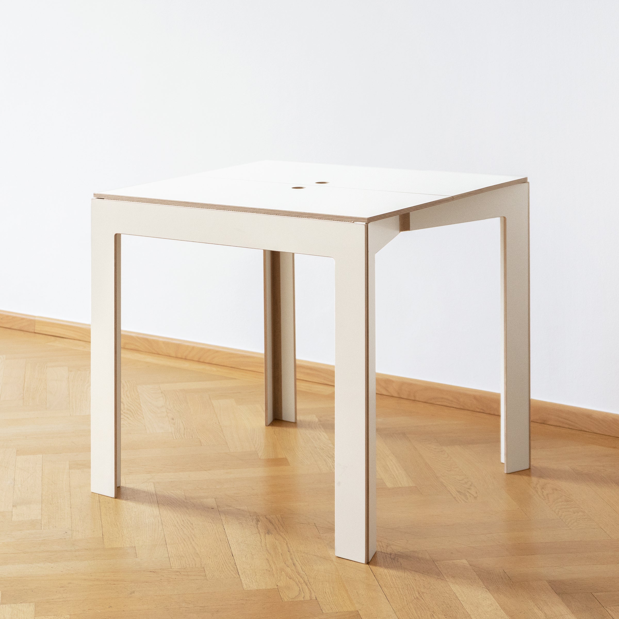 The Last Minute table by Moormann, made from birch plywood, features clean lines and a minimalist design with four legs. Its modern and space-saving style is accentuated when placed on a light wood parquet floor.
