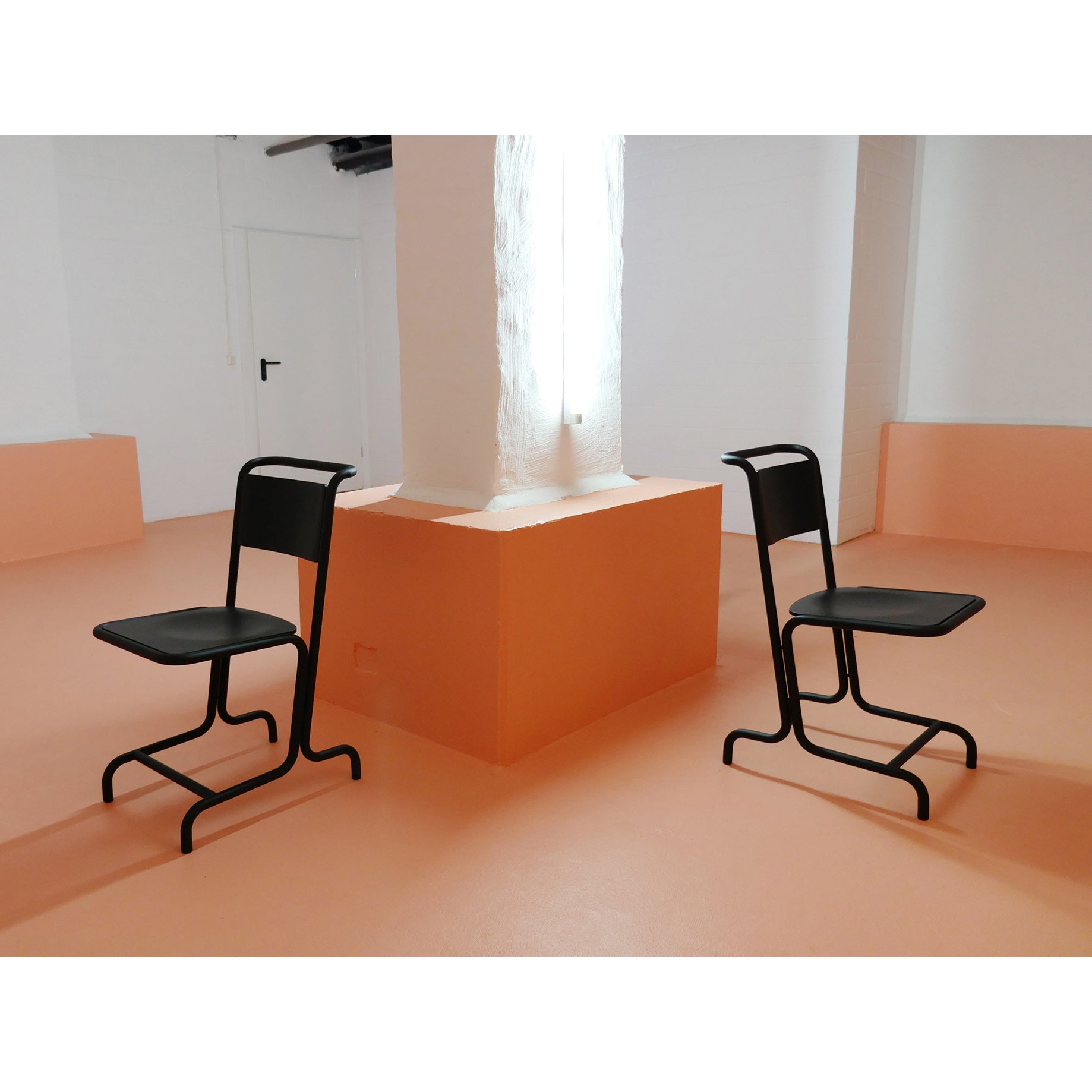 Two László Chairs from Atelier Haussmann face each other on an orange floor in a minimalist room. A large white column stands between them against peach-colored walls, creating a modern atmosphere with clean lines and a bright, uncluttered aesthetic that enhances seating comfort.