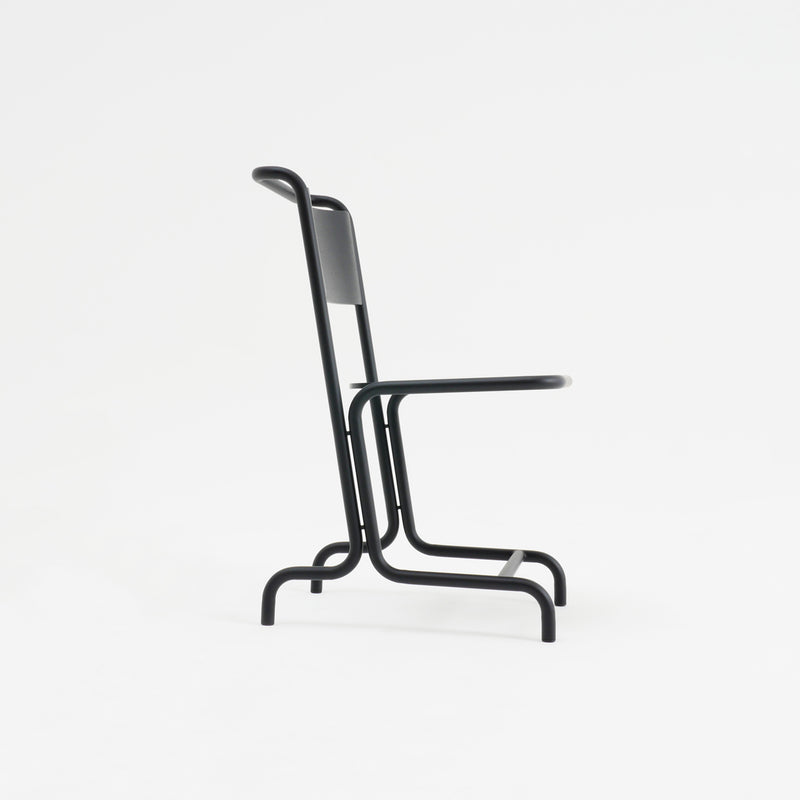 Side view of the László Chair by Atelier Haussmann, a minimalist black cantilever chair featuring a tubular metal frame and flat backrest. The sleek contemporary design on a plain white background highlights its elegant curved steel pipes for enhanced comfort.