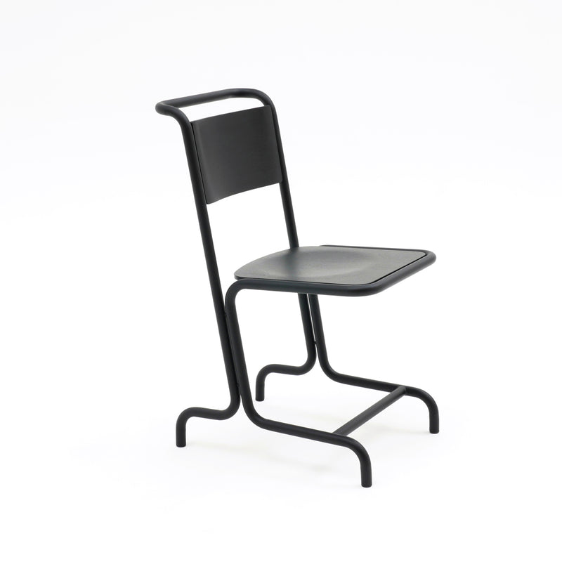 The László Chair by Atelier Haussmann is a modern cantilever chair with a minimalist design featuring a sleek metal frame, narrow backrest, flat seat, and curved steel pipe legs that connect at the base for a unique contemporary look and enhanced comfort against a white background.