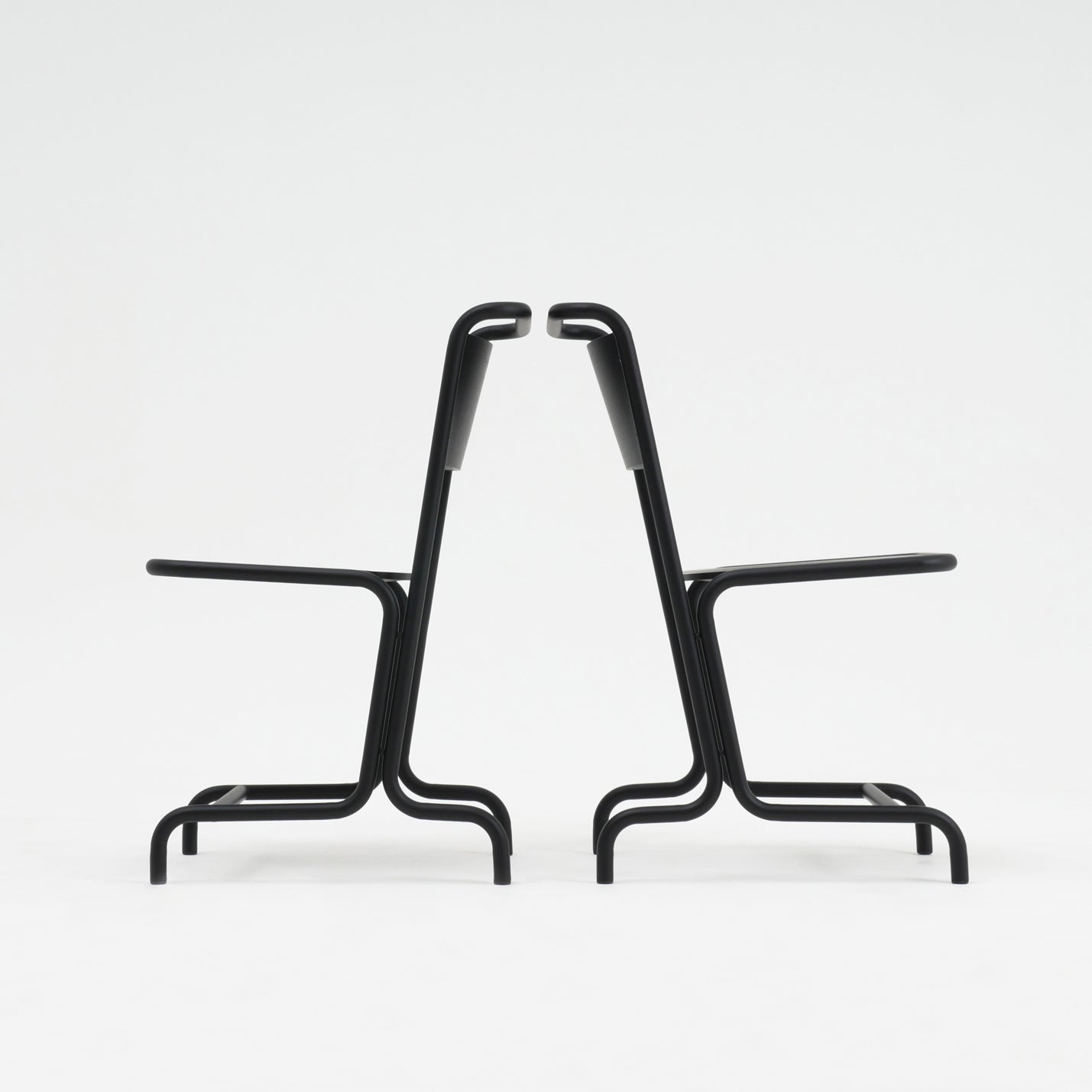 Two identical László Chairs by Atelier Haussmann, crafted from curved steel pipe, are positioned back-to-back on a white background, showcasing seating comfort with their symmetrical and minimalist black metal design.