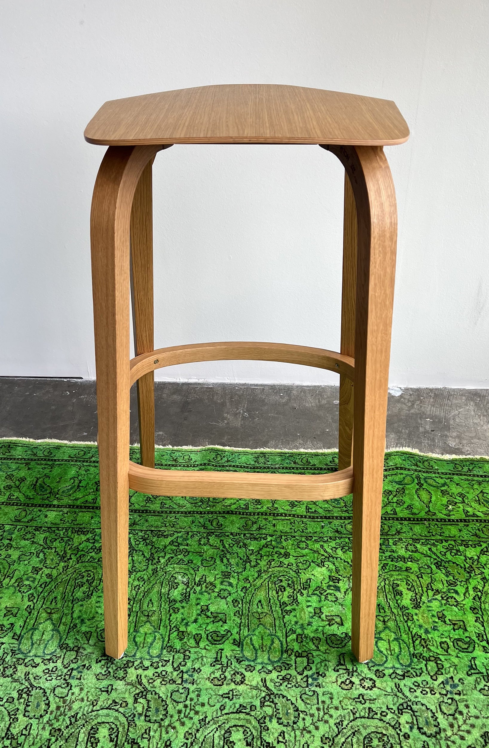 The Barstool Leaf by TON, featuring a slightly curved seat for ergonomic comfort, stands elegantly on a vibrant green patterned rug, against a plain white wall. (Sale).