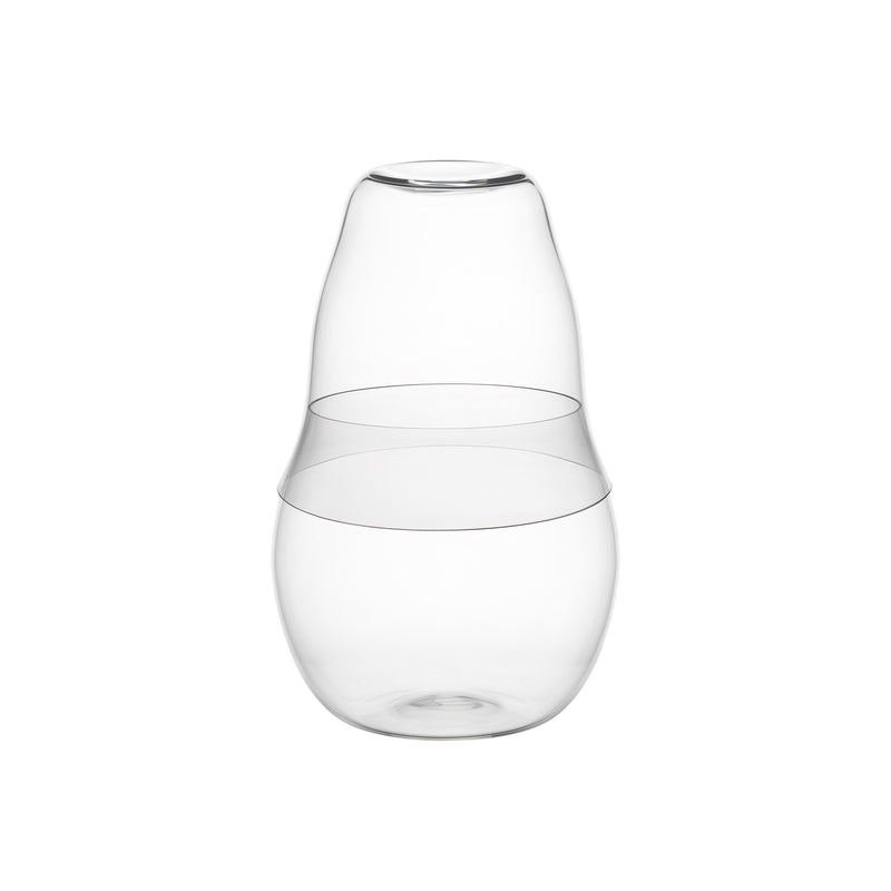 The Reigen Tumbler, a clear glass carafe by Aldo Bakker for Lobmeyr, features an elliptical shape with a wide bottom and narrow neck. Its minimalist top doubles as a detachable cup, inspired by Lobmeyrs elegant tumblers.