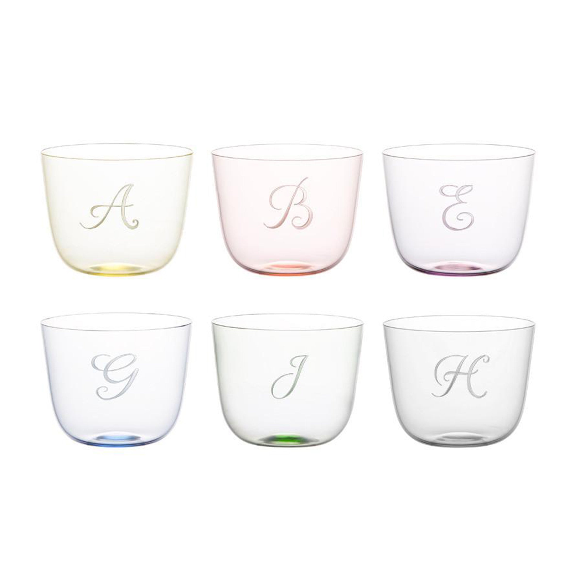A set of six pastel Alpha Water Tumblers by Lobmeyr, each engraved with a unique letter: A (yellow), B (pink), E (clear), G (blue), J (green), and H (light purple). Made from lead-free crystal, these mouth-blown glasses have a simple, translucent design and are effortlessly stackable.