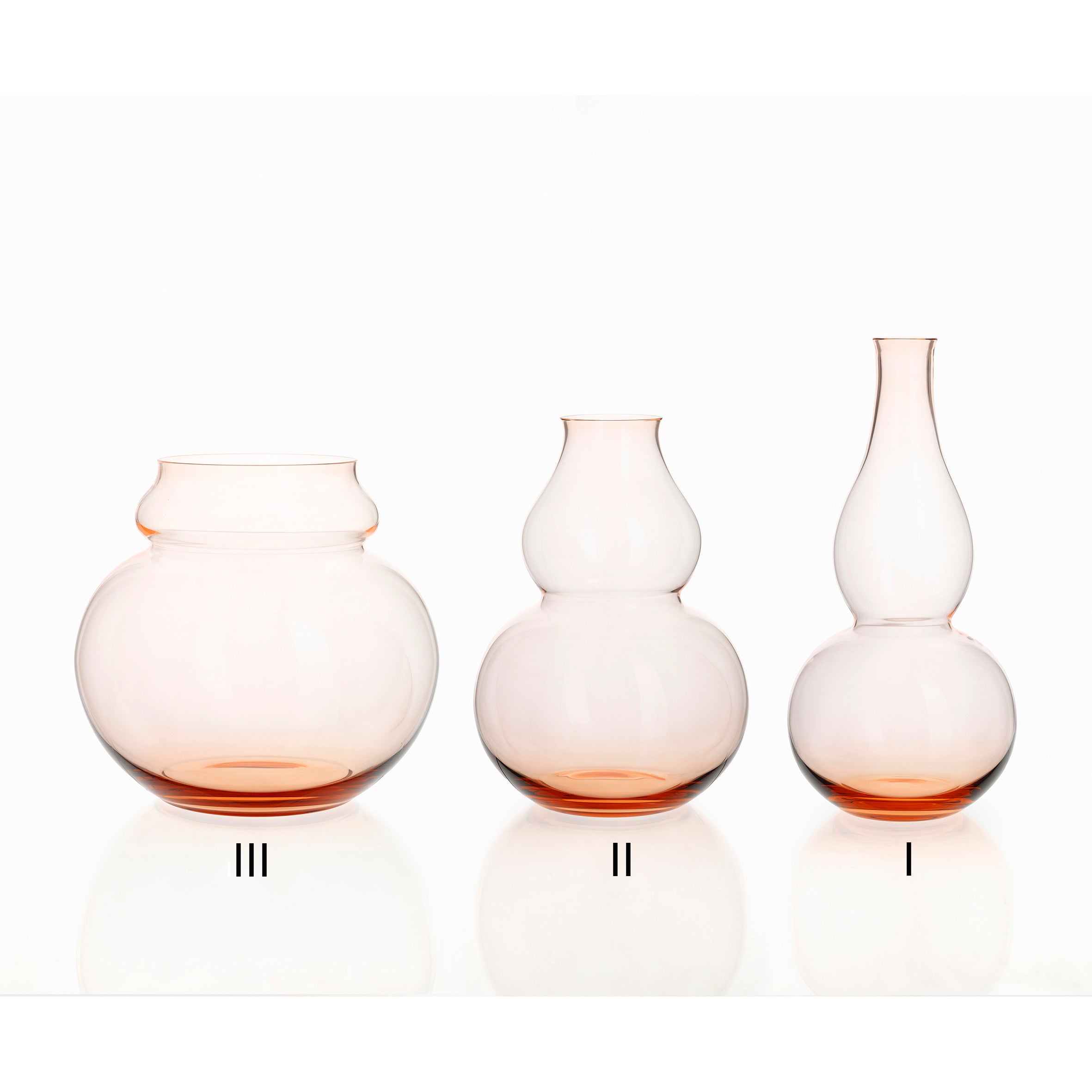 A trio of Lobmeyrs BV71 Calabash Flower Vases, crafted from mouth-blown lead-free crystal with vibrant orange bases, grace the white backdrop. Each vase features a distinctive silhouette: III on the left, II in the middle, and I on the right, all inspired by calabash gourds.
