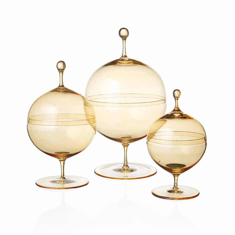 Three Candy Dish Gold Lustre pieces by Lobmeyr, featuring amber glass with rounded bodies and tapered lids on pedestal bases in various sizes. These mouth-blown, lead-free crystal dishes are translucent and reflect light beautifully, showcasing a design reminiscent of Oswald Haerdtls craftsmanship.