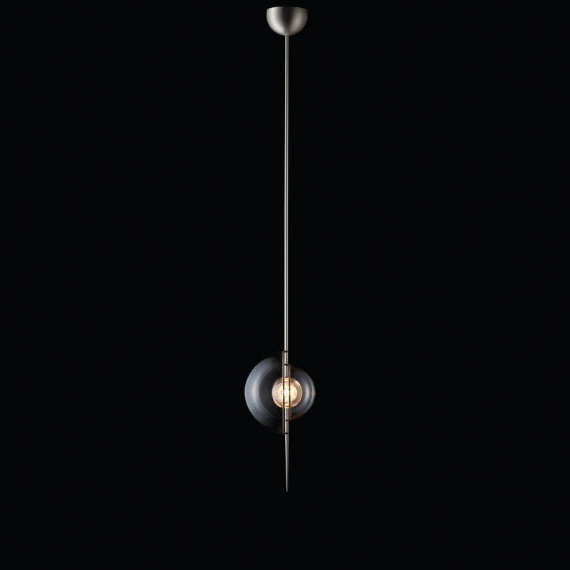 The Captured Pendant Lamp by Lobmeyr highlights minimalism with a long, thin metal rod and a lead-free crystal sphere encasing an exposed bulb set against a black background, exuding sleek elegance.