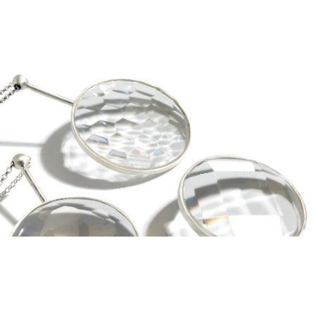 Close-up of three transparent, faceted Crystal Jellies by Lobmeyr, framed with silver metal and hanging on a chain. The crystal spheres cast elegant reflections and shadows on a white surface, showcasing expert glass-cutting techniques as they slightly overlap each other.