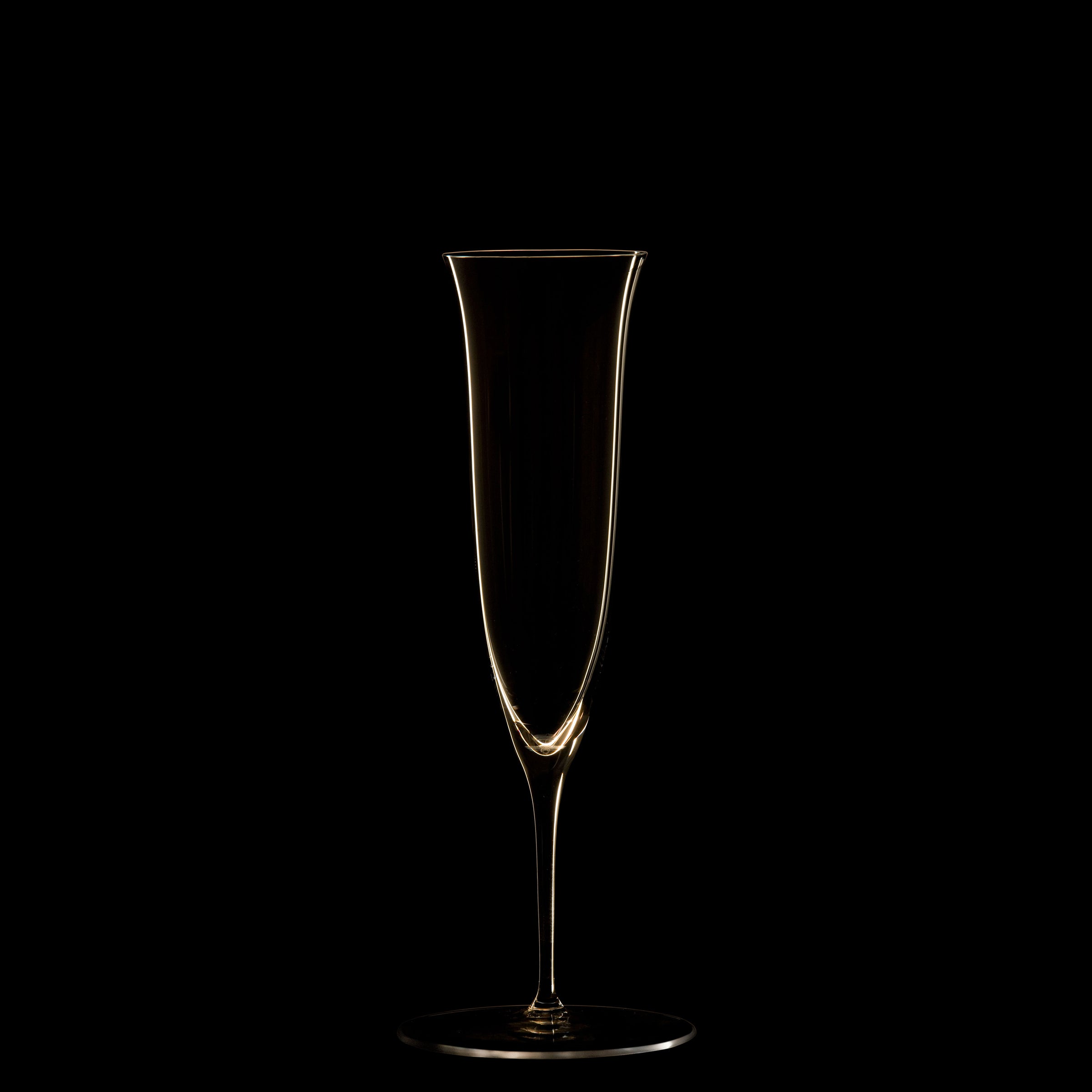 The tall, elegant crystal champagne flute from Lobmeyrs Drinking Set No. 238 - Patrician is crafted using mouth-blown techniques and stands against a black background, its golden outline echoing Josef Hoffmanns Wiener Werkstätte designs. The centrally positioned glass is empty.