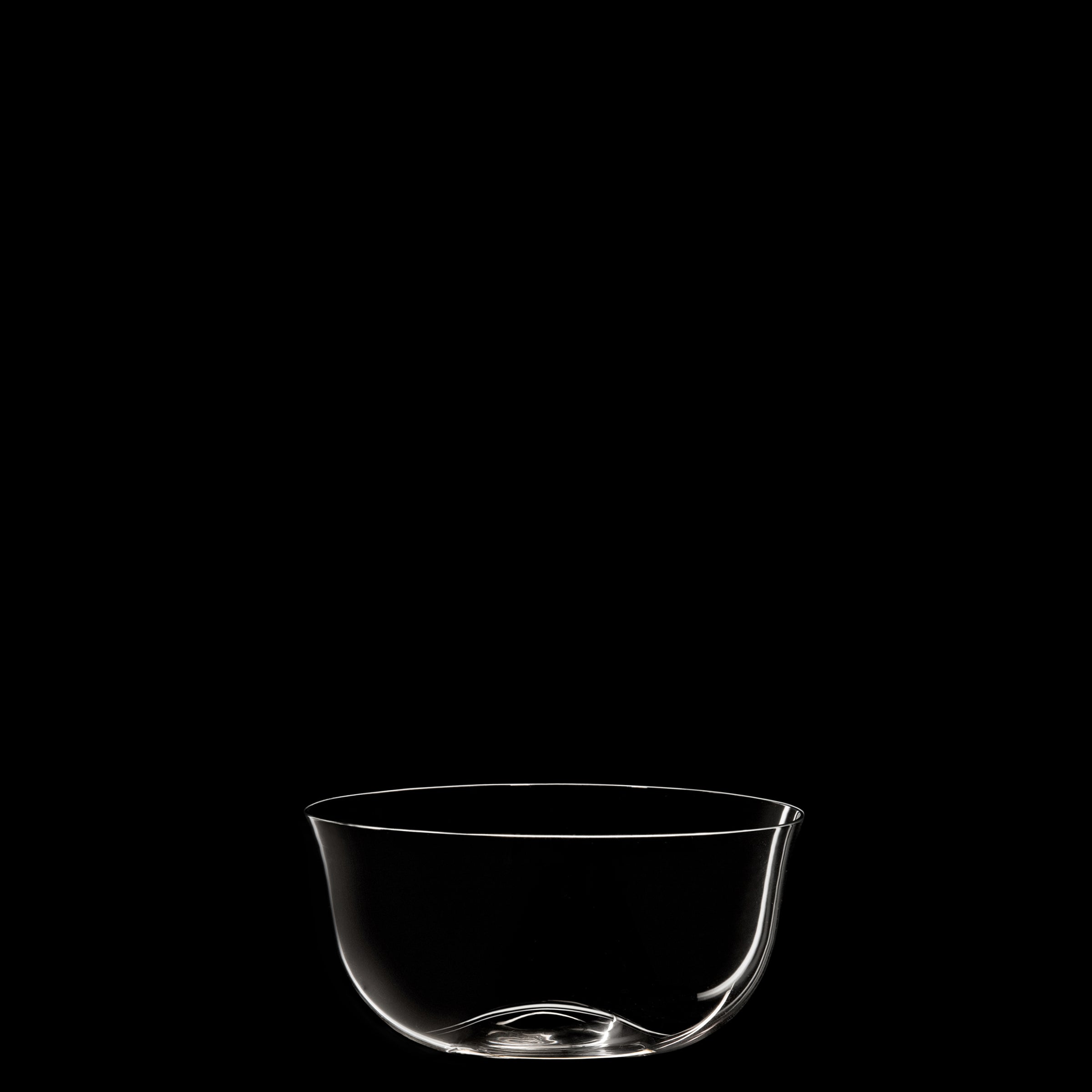 A clear glass bowl, reminiscent of Josef Hoffmanns Wiener Werkstätte designs, is centrally placed against a stark black background. This simplicity accentuates the delicate form and clarity of Lobmeyrs Drinking Set No. 238 - Patrician, echoing the artistry of mouth-blown crystal.