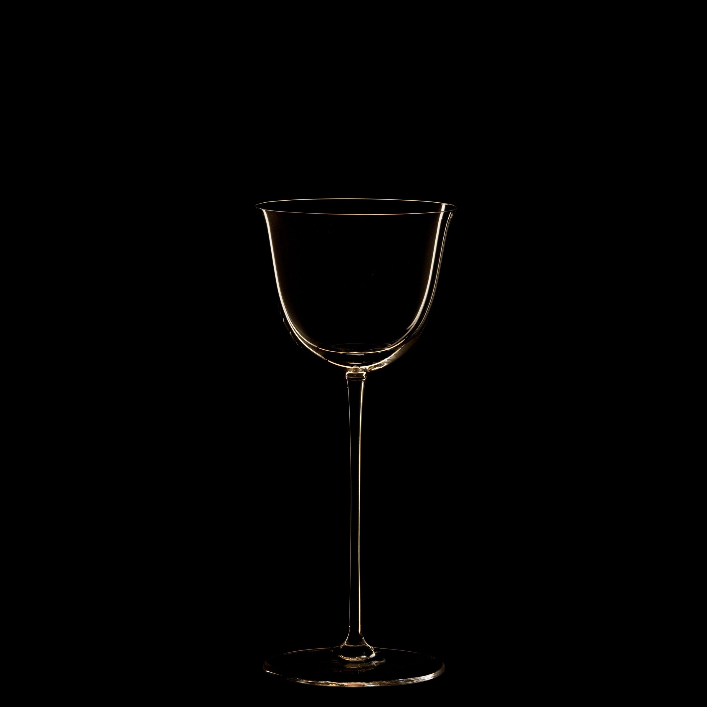 The Drinking Set No. 238 - Patrician from Lobmeyr features a transparent, long-stemmed wine glass centered against a black background. The mouth-blown crystal is softly illuminated, highlighting its elegant silhouette reminiscent of Josef Hoffmanns Wiener Werkstätte designs.