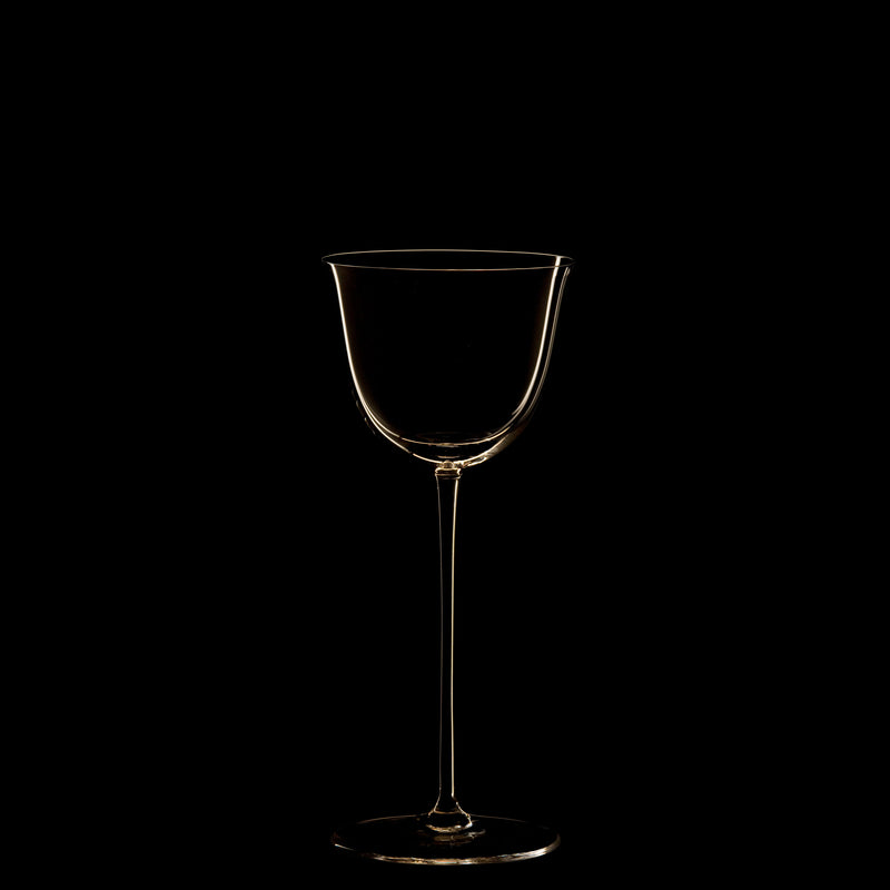 The Drinking Set No. 238 - Patrician from Lobmeyr features a transparent, long-stemmed wine glass centered against a black background. The mouth-blown crystal is softly illuminated, highlighting its elegant silhouette reminiscent of Josef Hoffmanns Wiener Werkstätte designs.
