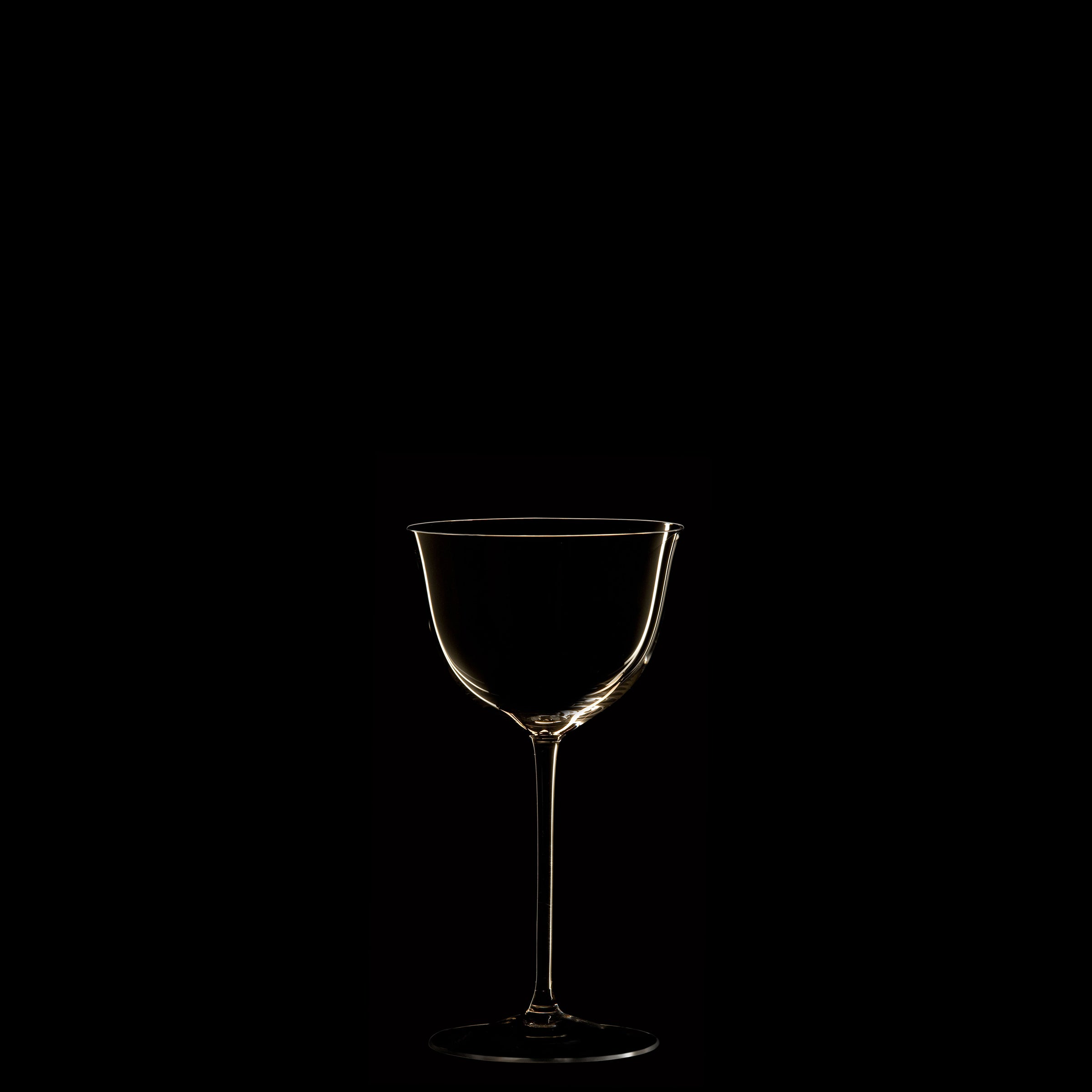 A mouth-blown crystal wine glass from Lobmeyrs Drinking Set No. 238 - Patrician, elegantly lit from one side, casts a subtle glow on its contour against a black background, echoing the timeless elegance of Wiener Werkstätte design.