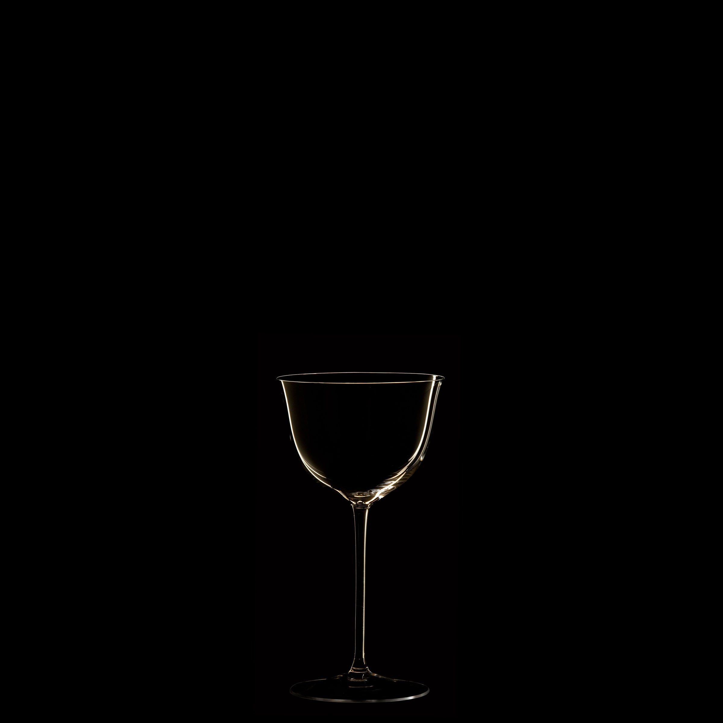 A thin-stemmed wine glass silhouette from Lobmeyrs Drinking Set No. 238 - Patrician evokes Josef Hoffmanns Wiener Werkstätte designs against a black background, highlighted by subtle golden reflections along its contours.