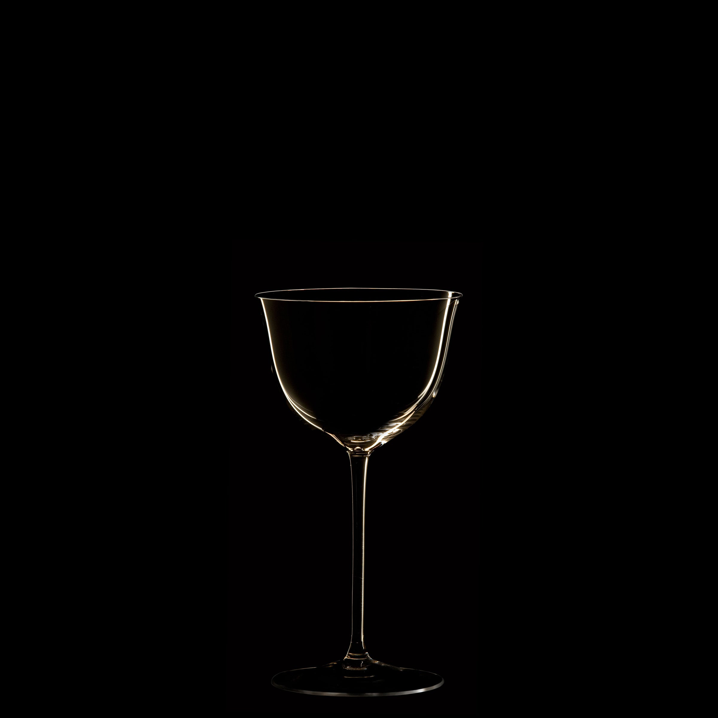Against a black background, the Drinking Set No. 238 - Patrician by Lobmeyr features a wine glass crafted from mouth-blown crystal, accented by soft highlights outlining its elegant contours and stem, embodying Josef Hoffmanns Wiener Werkstätte style.