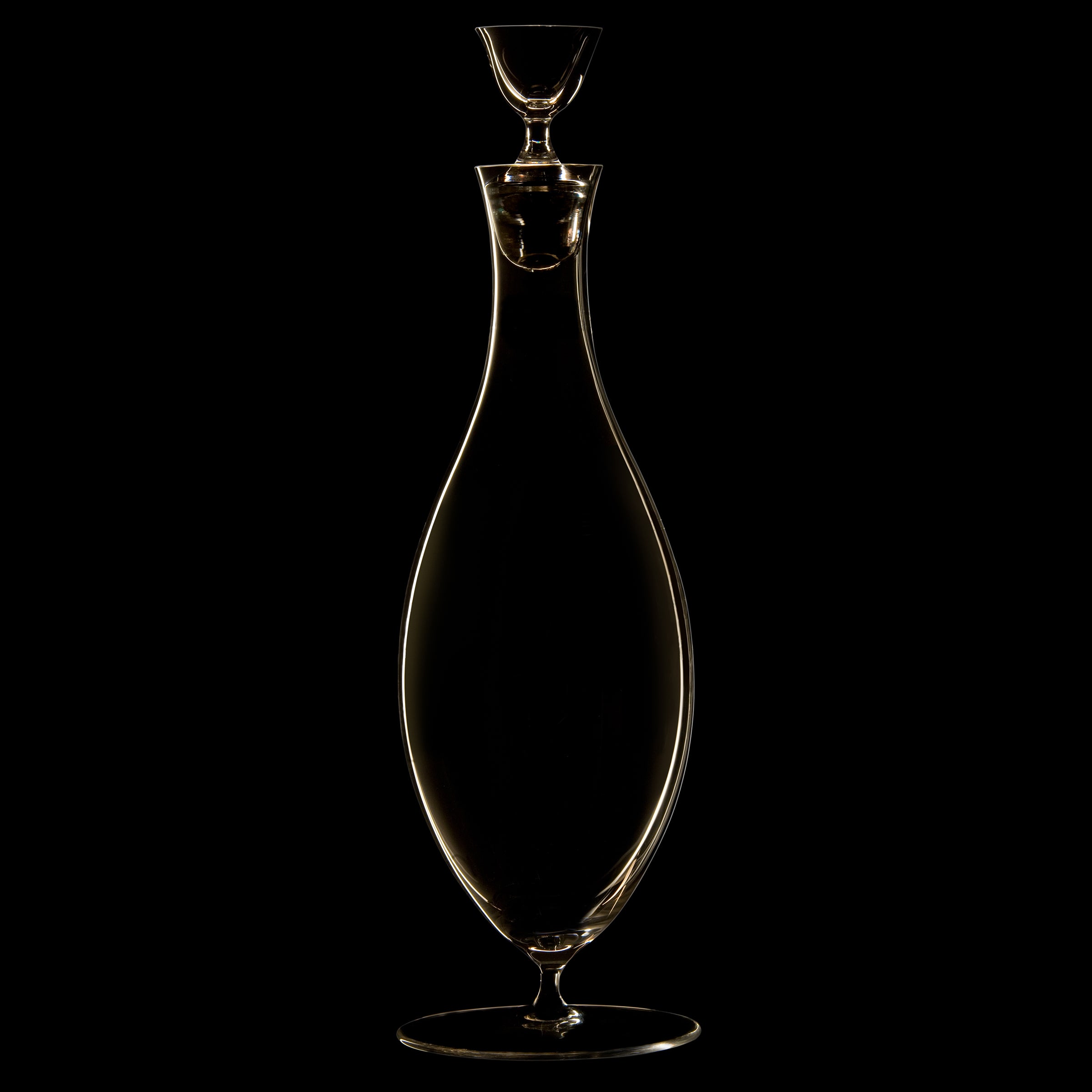 The Drinking Set No. 238 - Patrician by Lobmeyr is a slender, elegantly curved glass decanter crafted from mouth-blown crystal, complete with a stopper. Its smooth contours reflect against a black background, echoing the refined aesthetic of Josef Hoffmann and the Wiener Werkstätte movement.