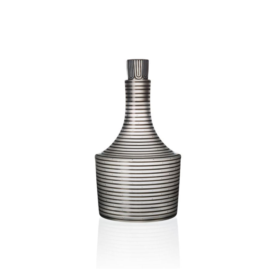 The Lobmeyr Drinking Set Serie A features a mouth-blown crystal glass bottle with a short neck and wide base. It is adorned with horizontal black stripes, offering a modern textured look, and its reflective base contrasts elegantly against a white background.