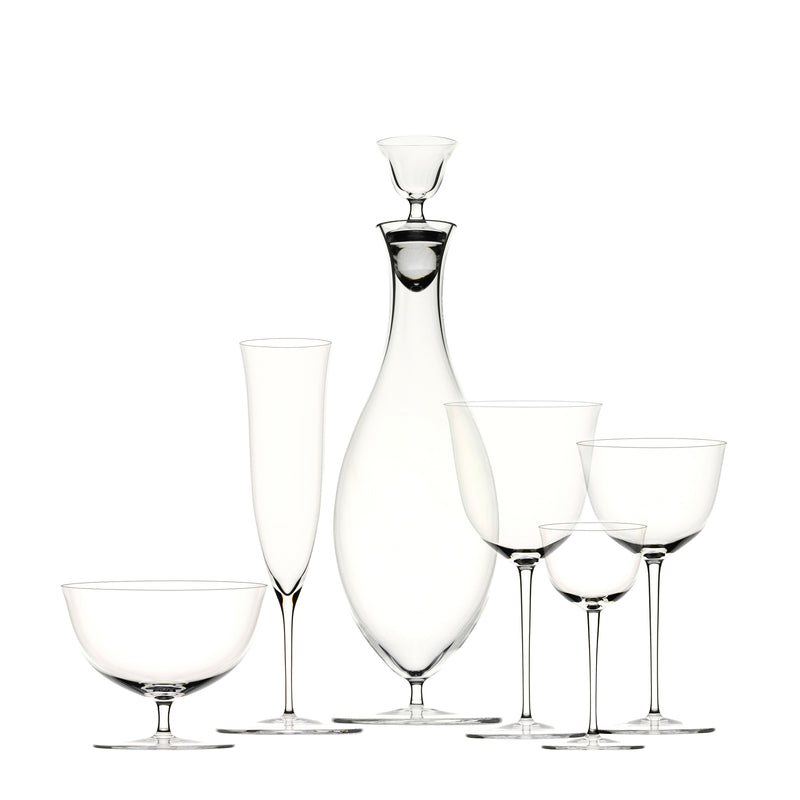 The Drinking Set No. 238 - Patrician by Lobmeyr features a tall, slender decanter with a stopper, surrounded by wine glasses and a champagne flute, set against a plain white background. This clear, mouth-blown crystal glassware echoes Josef Hoffmanns elegant design ethos for the Wiener Werkstätte.