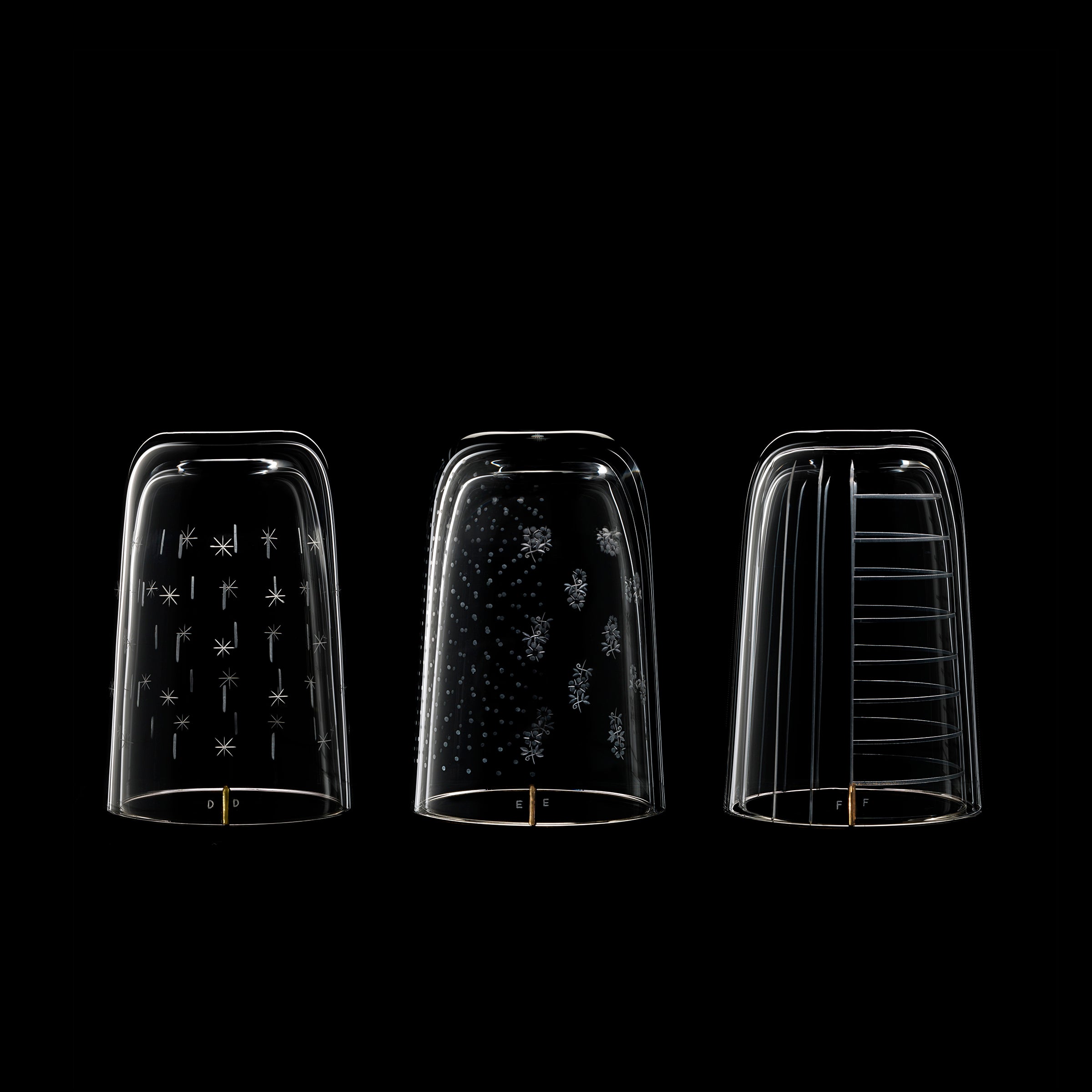 Three transparent glass domes set against a black background echo the craftsmanship of Lobmeyrs Drinking Set No. 284 Alphabet, featuring unique white patterns—abstract shapes, dots, and lines—adding intricate detail like ornate wine glasses in an elegant table setting.