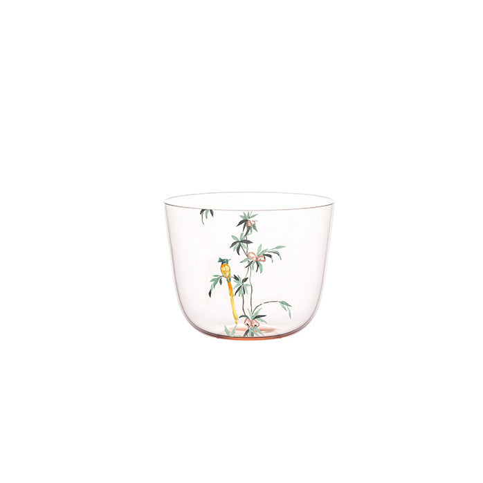 The Alpha Water Tumbler by Lobmeyr showcases delicate hand-painted floral and bamboo designs, evoking a Garden of Paradise. The clear glass cup features pink flowers and green foliage, offering an elegant touch against a white background.