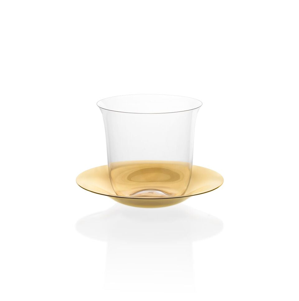 A clear teacup from Lobmeyrs Lily Tea Set sits on a glossy golden saucer against a plain white background. The saucers reflective surface enhances its metallic sheen, showcasing the elegance of this set.